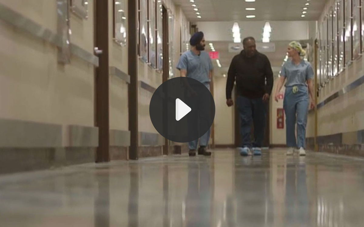 Still from Video. Pete, Dr. Singh, Samantha and patient Robert walking down a hall in a hospital coming toward the camera.