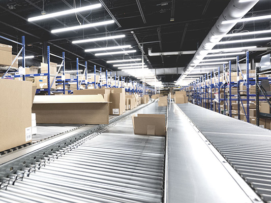A box travels on a conveyor belt through a large warehouse.