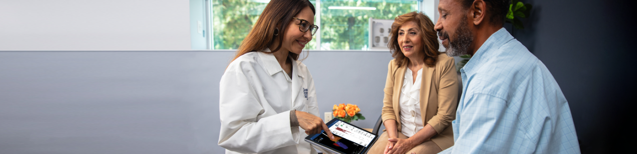 Physican points at tablet with Boston Scientific's Vercise Neural Navigator 5 Software while a patient and caregiver look on.