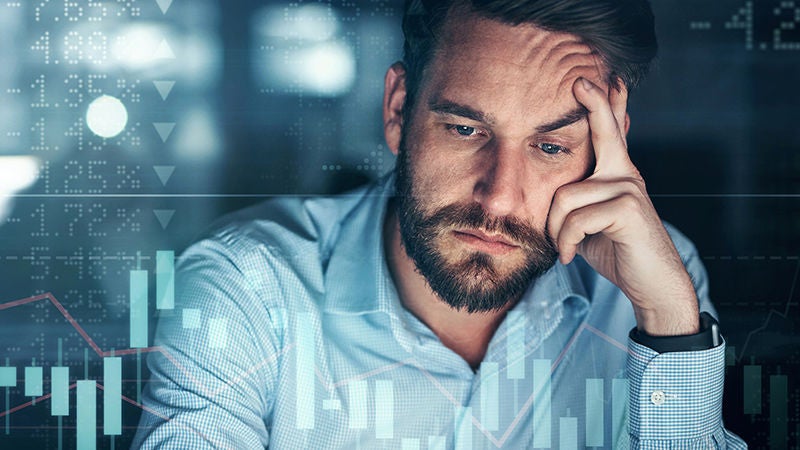Stressed man reviewing financial charts and market data on a computer screen
