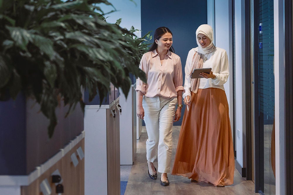 Two employees walking together through an office corridor.