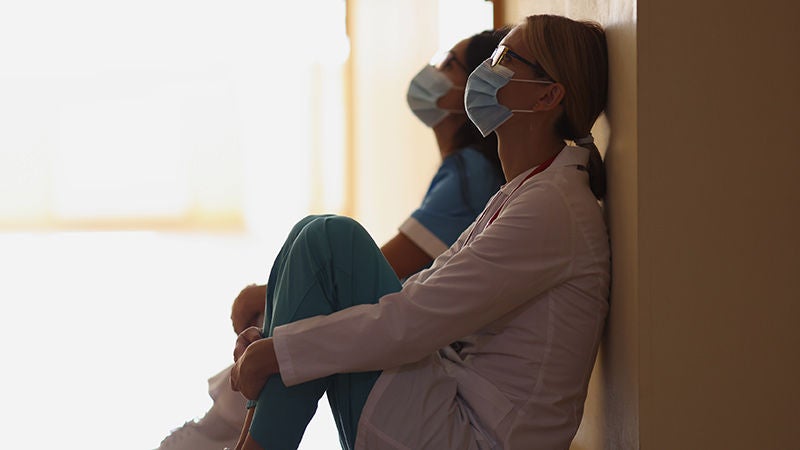 Exhausted nurses wearing a face mask sitting on a hospital floor during a medical emergency