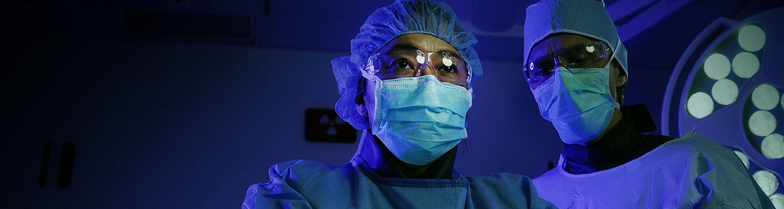 Two surgeons in operating room wearing blue masks.
