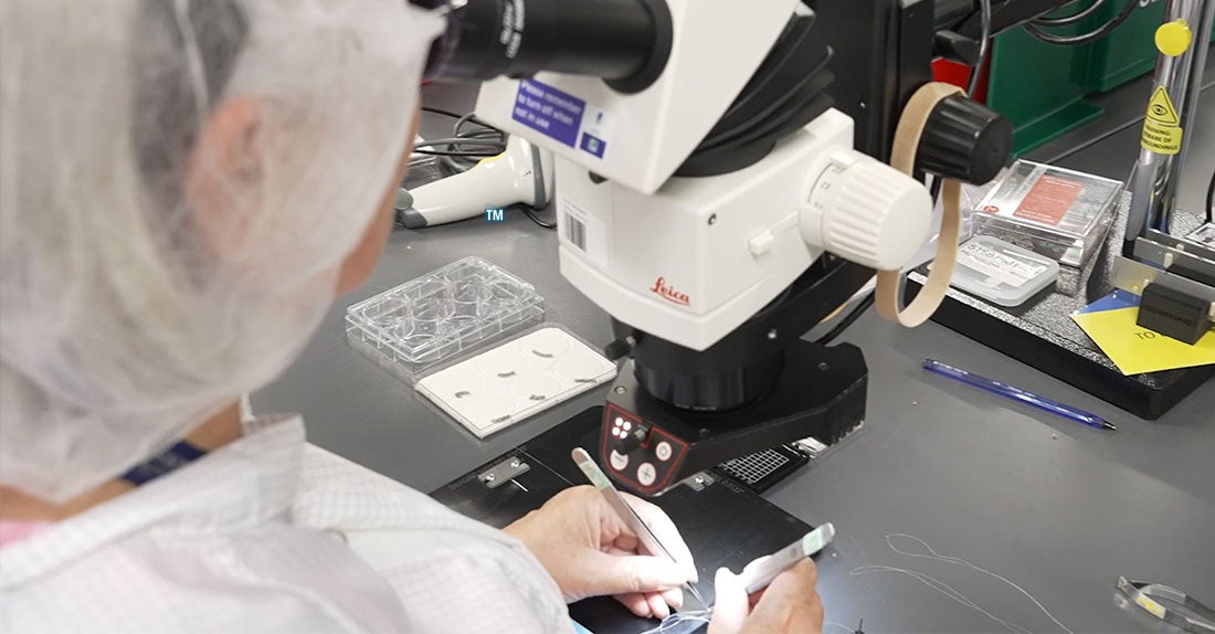 Technician reviewing specimen under microscope.