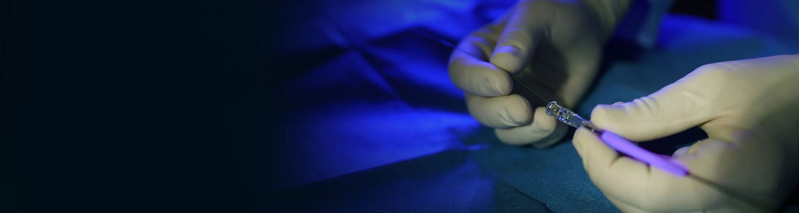 Gloved hands connecting a catheter device on a surgical field.