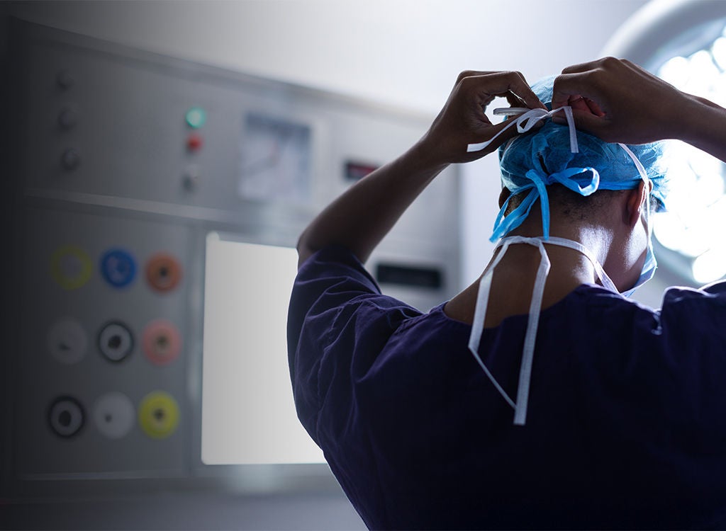 Healthcare professional tying a surgical mask around their scrub cap in an operating room.
