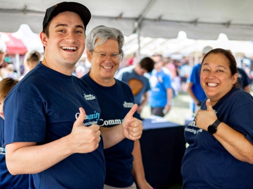 A group of employees in matching blue shirts pose at the check-in tent of a charity walk event.