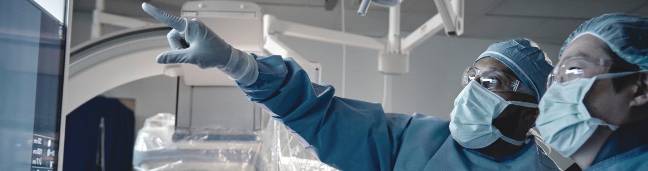Two physicians looking at a monitor, arms distance away in the OR with one physician pointing at it.