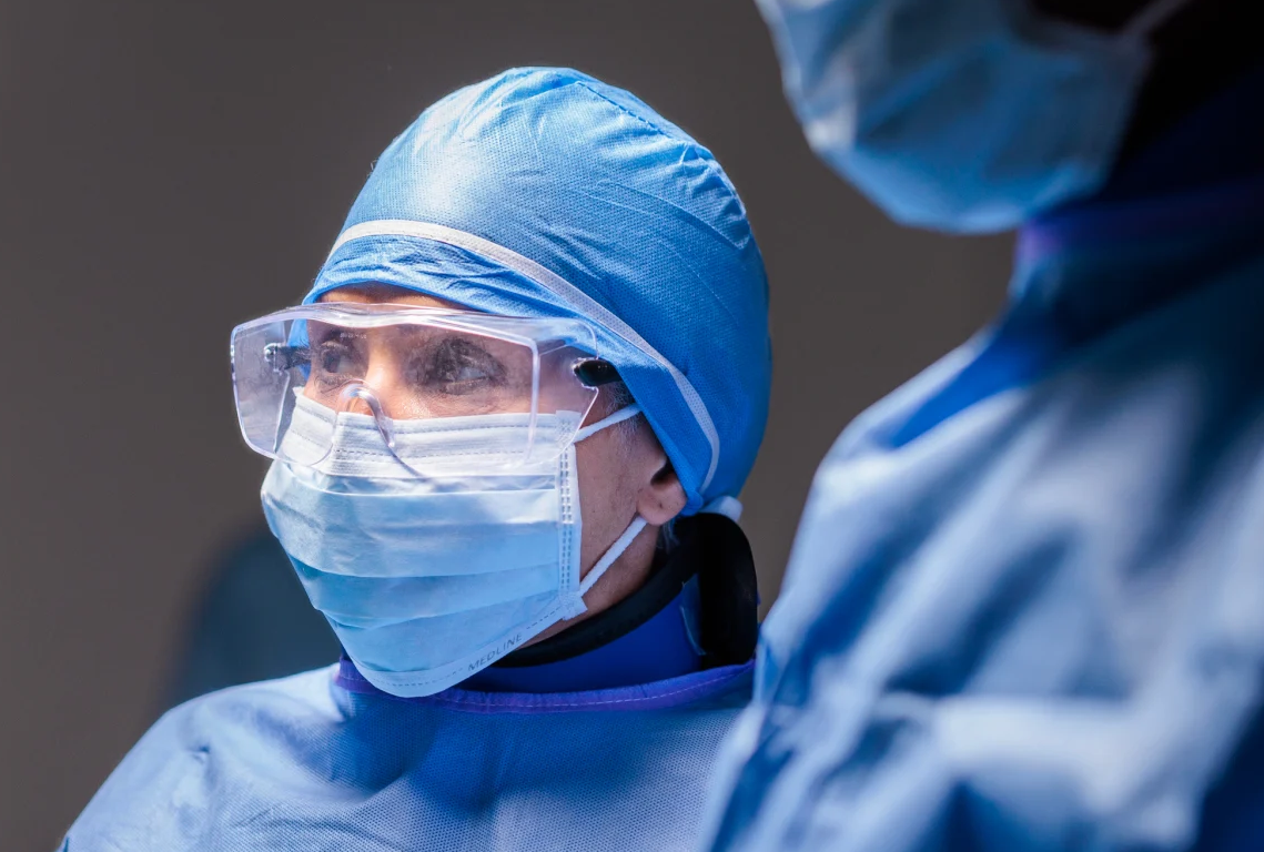 Healthcare professionals in protective surgical attire beside medical imaging equipment. 