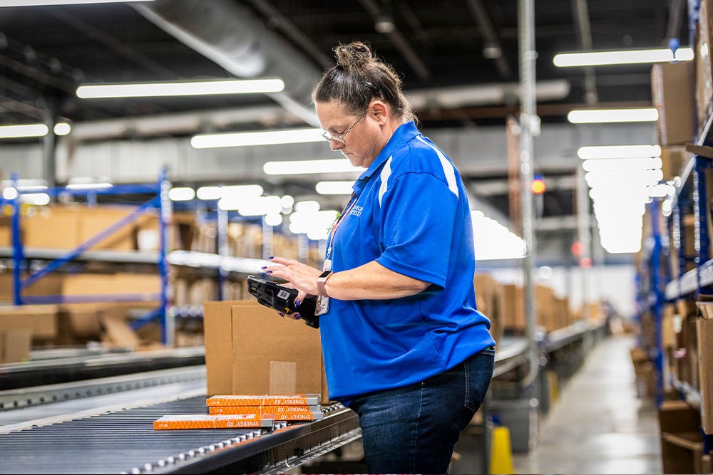 Warehouse worker scanning boxes on conveyor line.