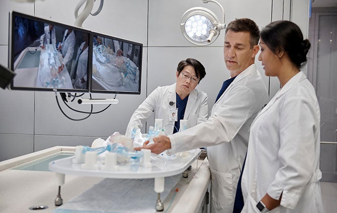 Three medical professionals at a table with monitors analyzing research.