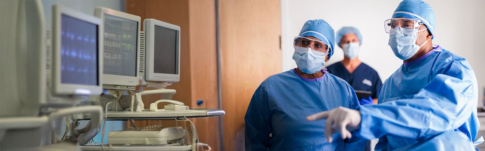 A woman and a man wearing protective gear look into a monitor.