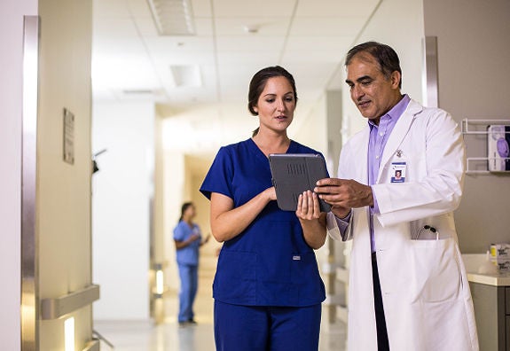 Doctor and nurse reviewing patient information on a tablet in a hospital hallway.