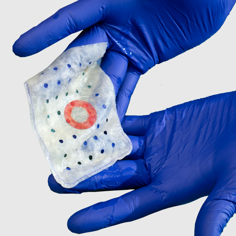 Gloved hand holding a sealed envelope containing a CIED with a visible red circular ring of antibiotics. 