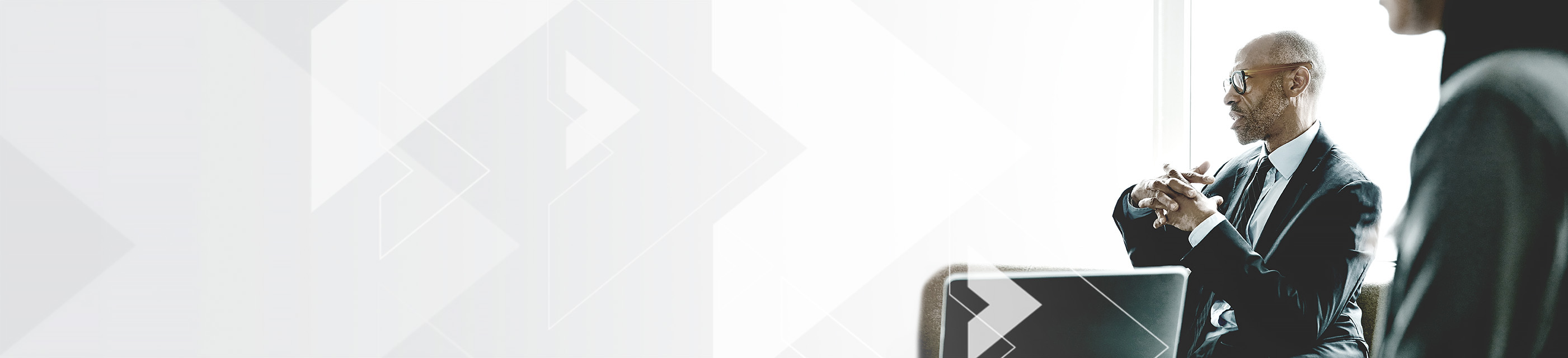 Businessman wearing suit with hands folded, with another businessperson in the corner.