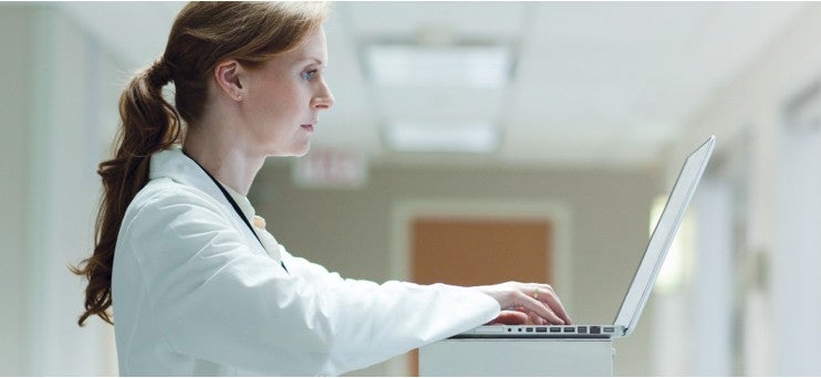 Woman wearing lab coat working on laptop.
