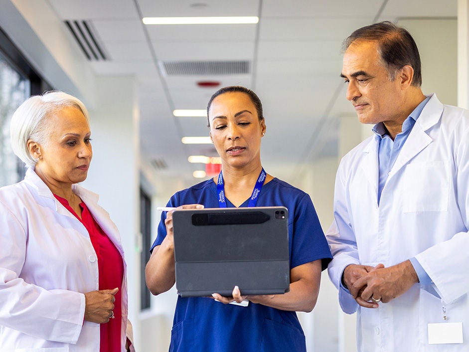 Three clinicians reviewing information on a tablet in a hospital corridor.