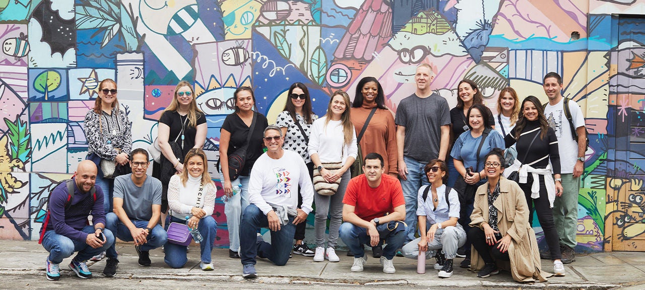 A team of Social Change Champions participants pose on a sidewalk in front of a large mural that covers a wall.