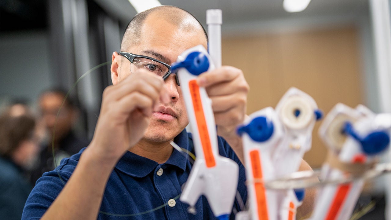 Manufacturing specialist inspecting medical device components and team discussion in a production environment.
