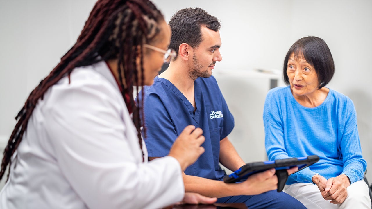 A healthcare professional and a medical staff member sit with a patient during a consultation.