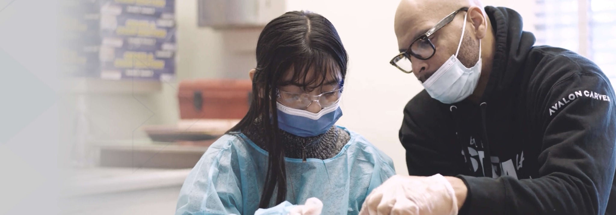 A man in mask sitting with young girl and giving instruction.