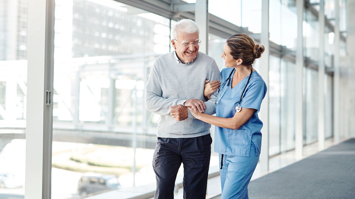 Healthcare worker assisting senior patient in hospital corridor to improve patient satisfaction