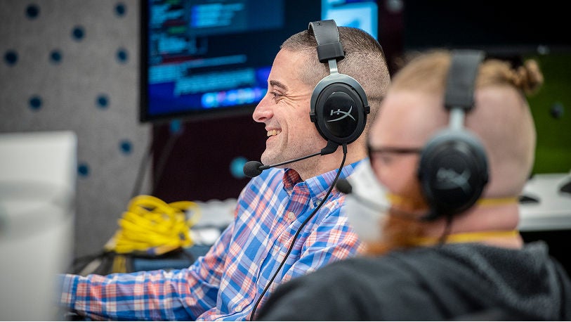 Two people wearing over-ear headsets work at computer stations in a modern office. 