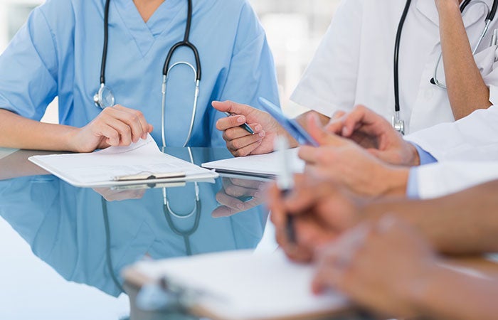 Three physicians sitting at a table, focused only on their hands and papers in front of them. 