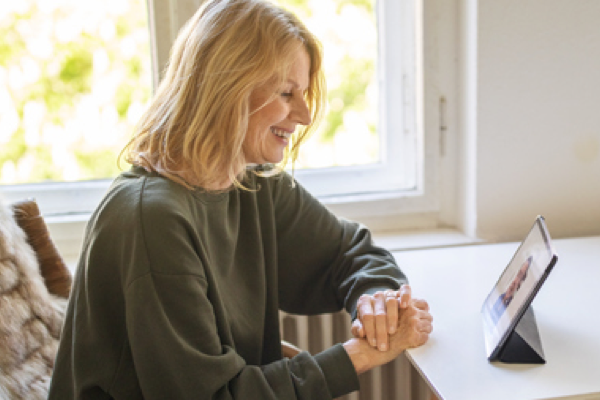 Woman smiling and looking at tablet on table, in a tele-psych evaluation.
