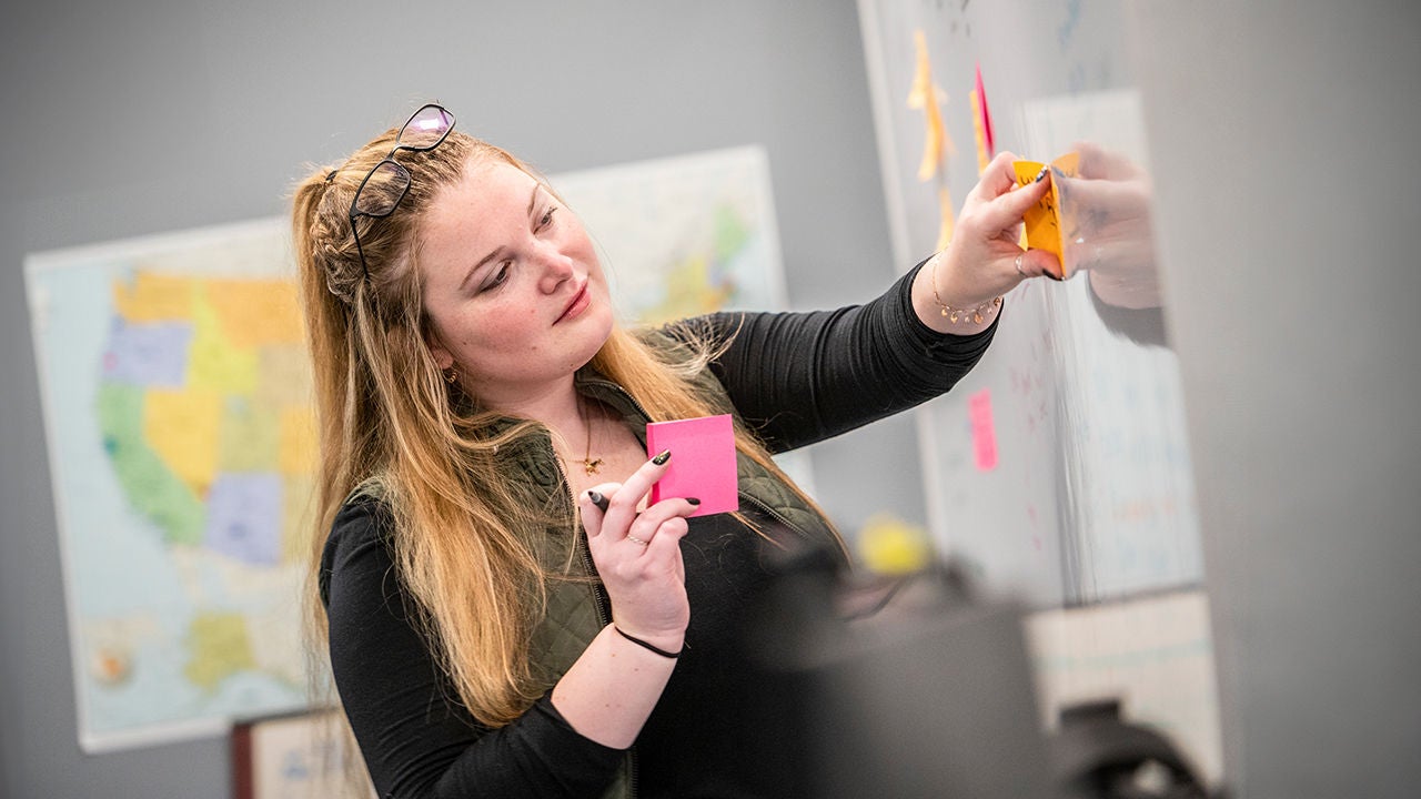 Woman brainstorming with sticky notes on board.