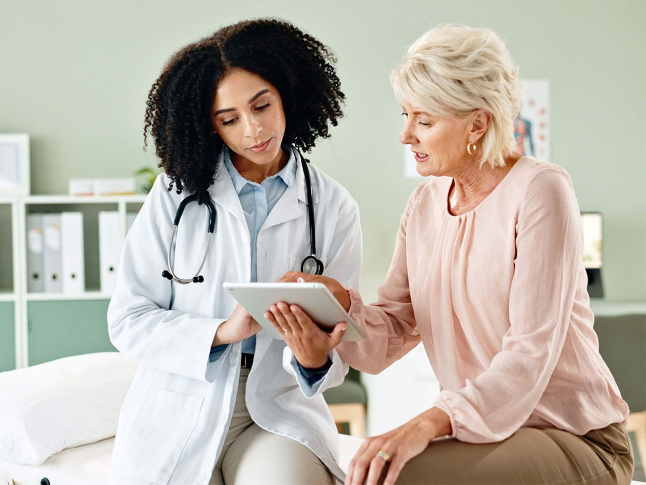 Physician holding tablet talking to a patient.