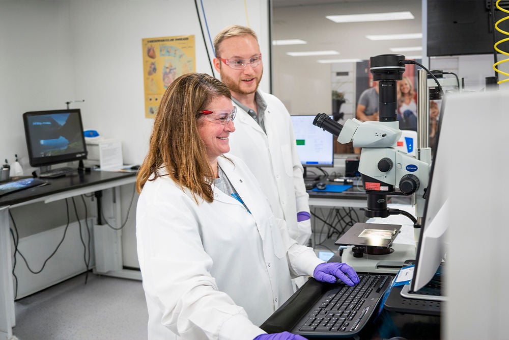 Two laboratory scientists in white lab coats work together at a computer workstation.
