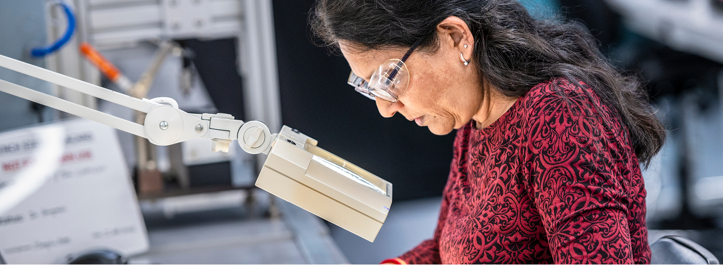 Employees collaborating in a meeting and technician inspecting components under magnification.
