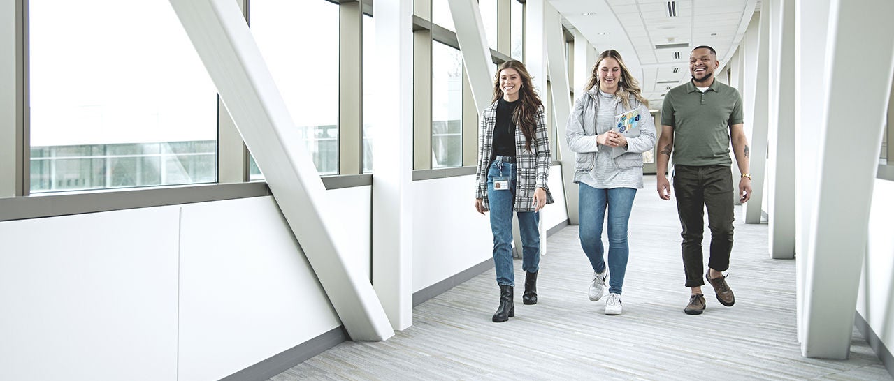 Three racially diverse employees laugh together while walking down a hallway.
