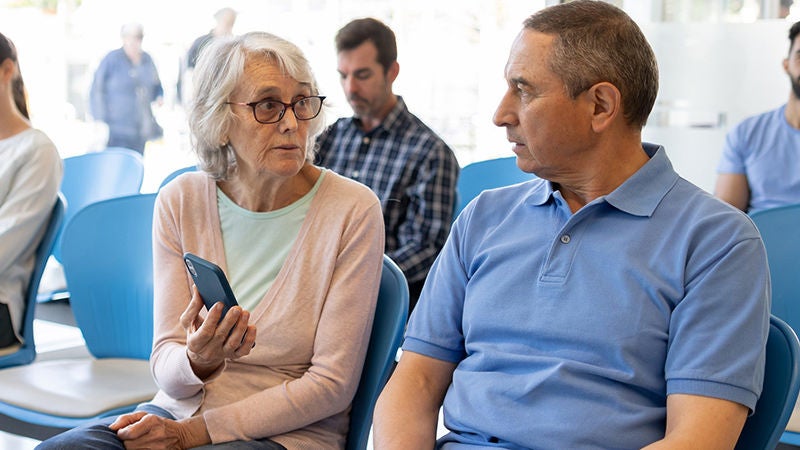 Older couple waiting in a hospital reception discussing a healthcare appointment