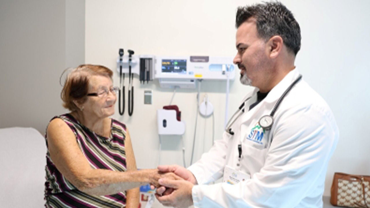 Doctor holding an elderly patient’s hand during a consultation in a medical clinic.