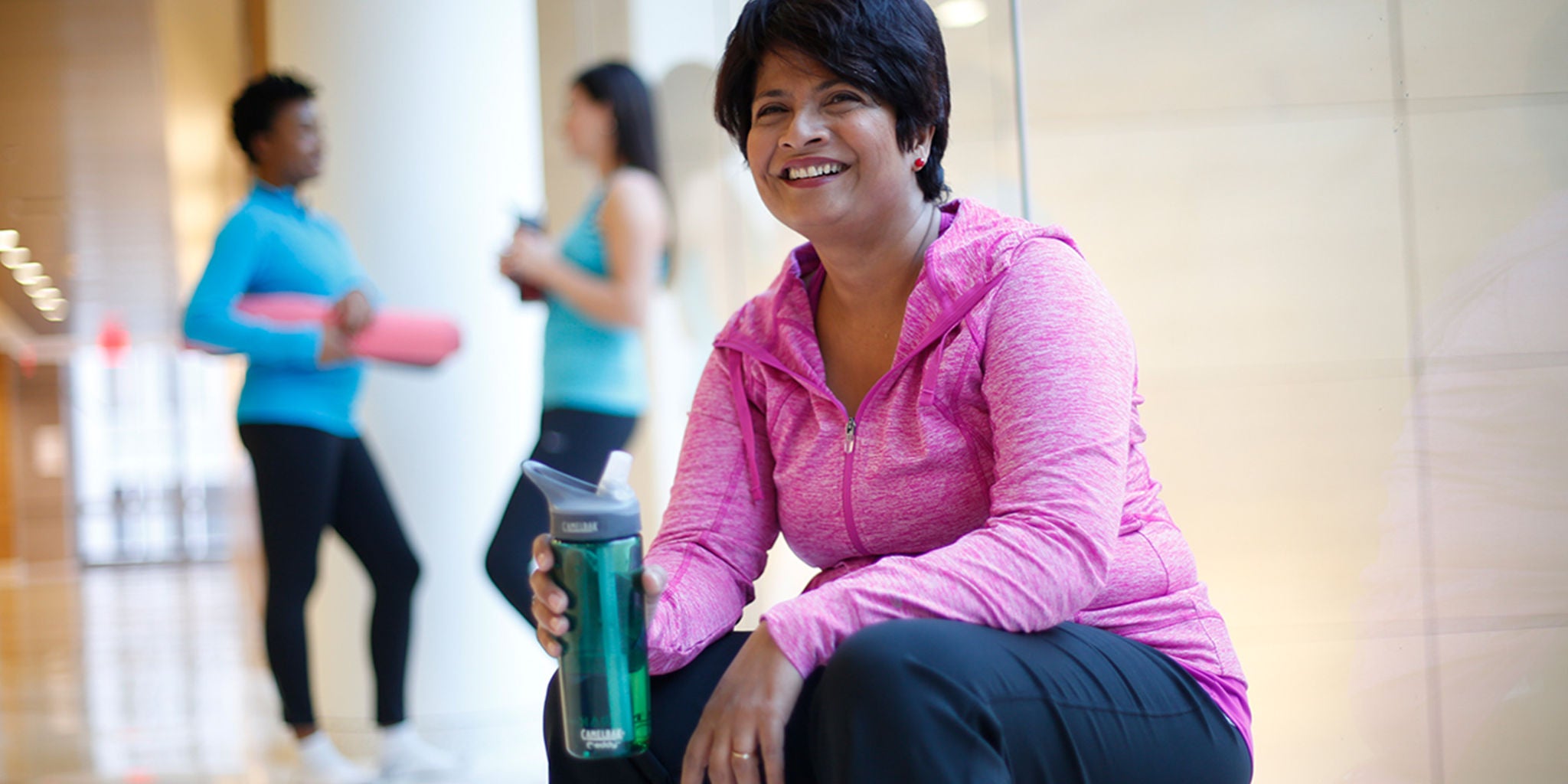 Women sitting on exercise ball with two women talking in background.