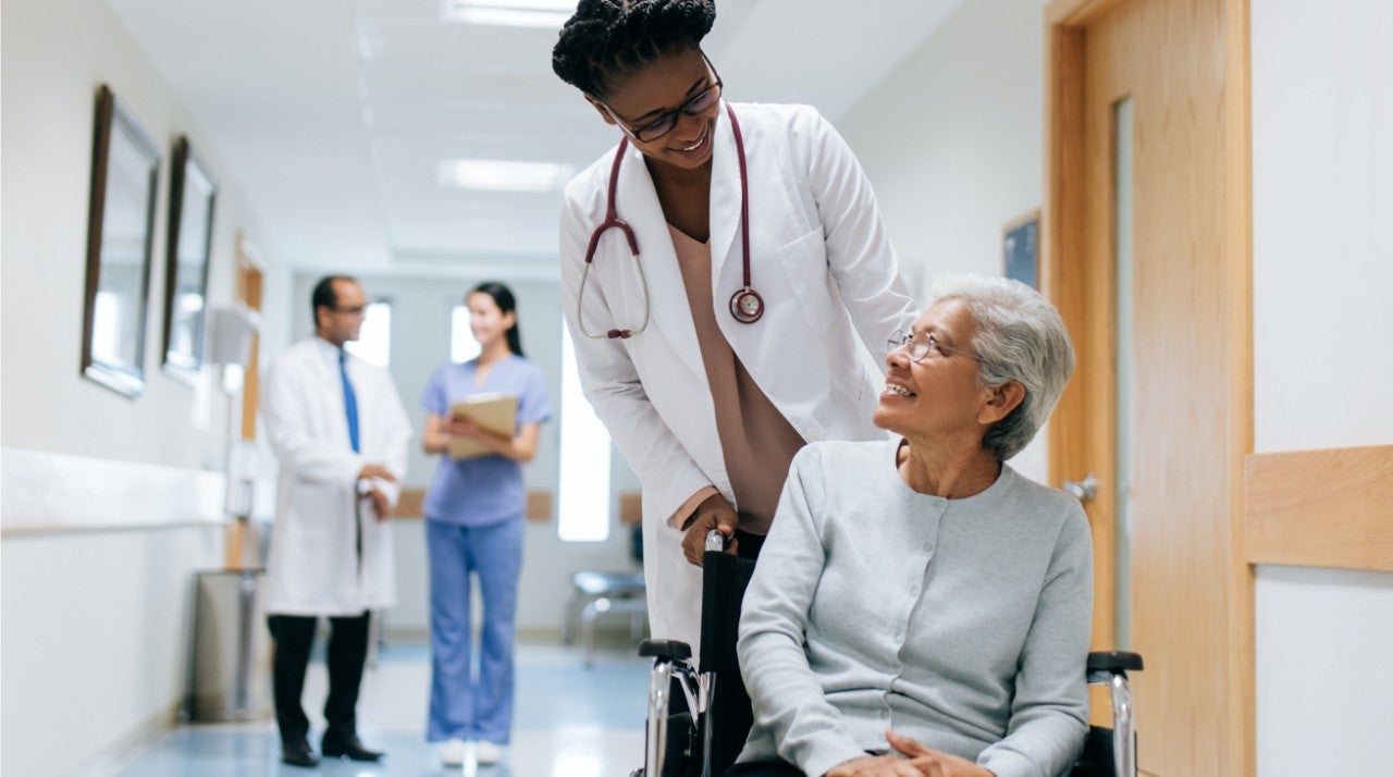 Medical professional helping a paitent in a wheelchair down a hallway.