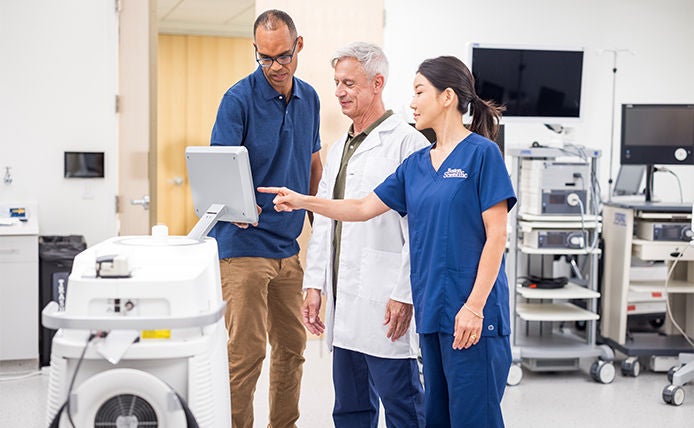 Healthcare professionals reviewing and operating a medical device in a clinical procedure room.