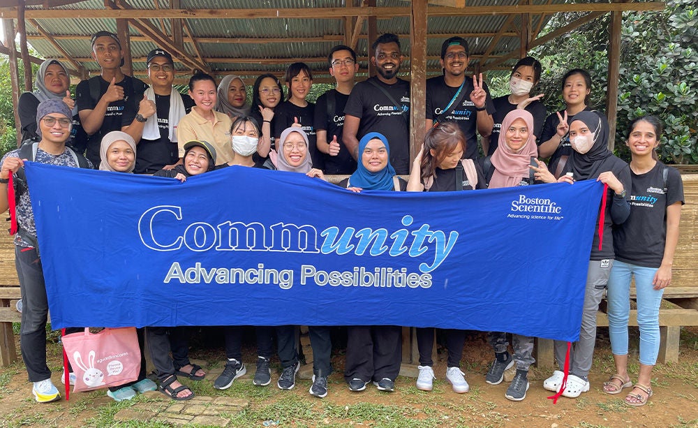 Group of smiling people holding Boston Scientific community banner.