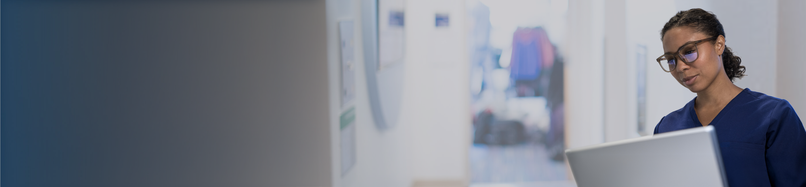 Healthcare professional reviewing information on a laptop in a hospital hallway.