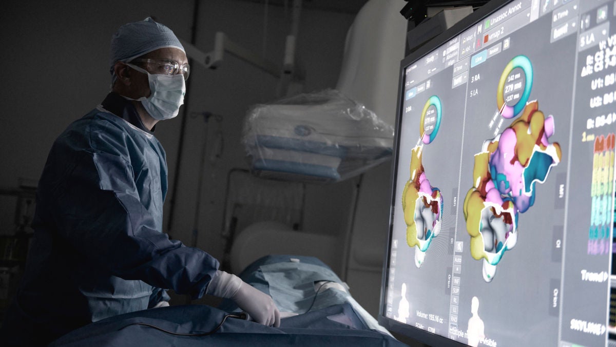 physican in mask and lab coat examin patient with help of large monitor.
