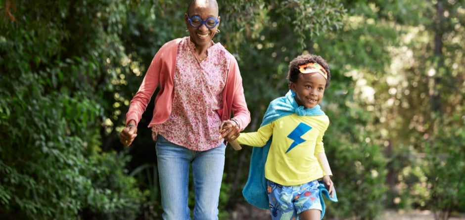 A smiling grandma running and playing with her granddaughter in a yard.
