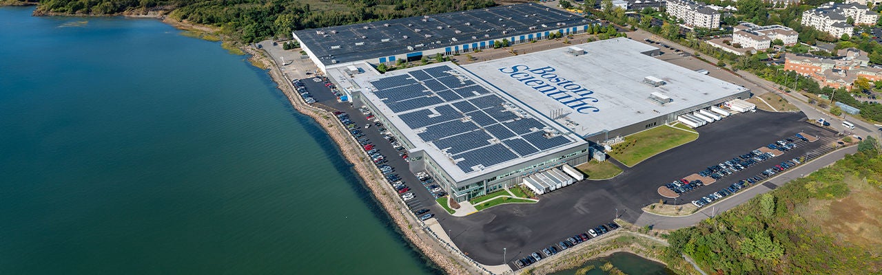 A large industrial facility is captured from an aerial perspective beside a body of water. 
