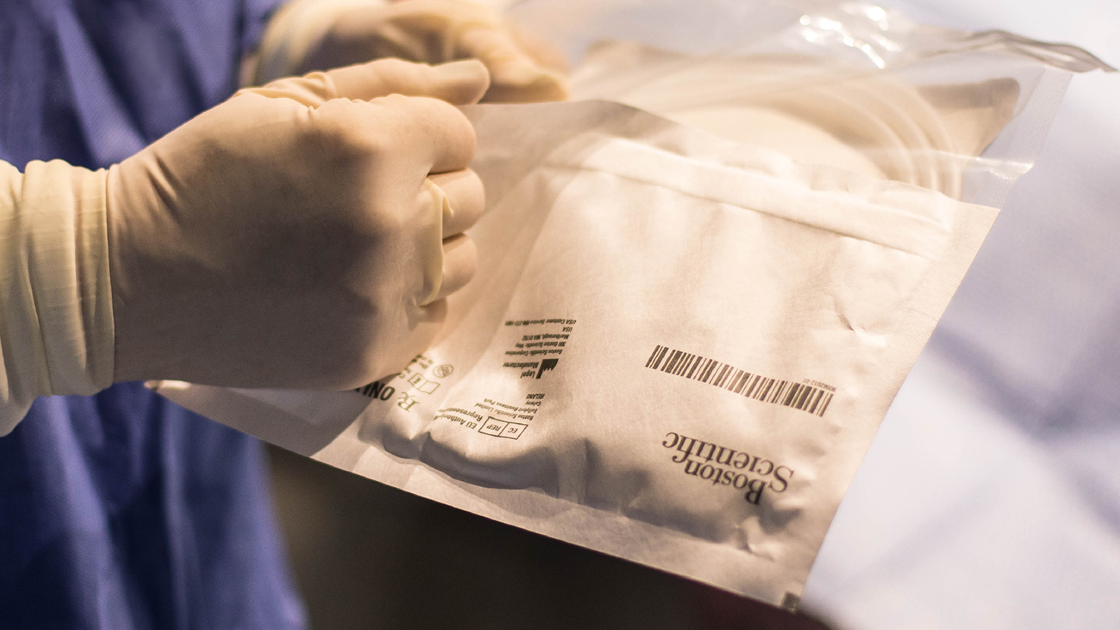 Gloved hand holding Boston Scientific product packaging.