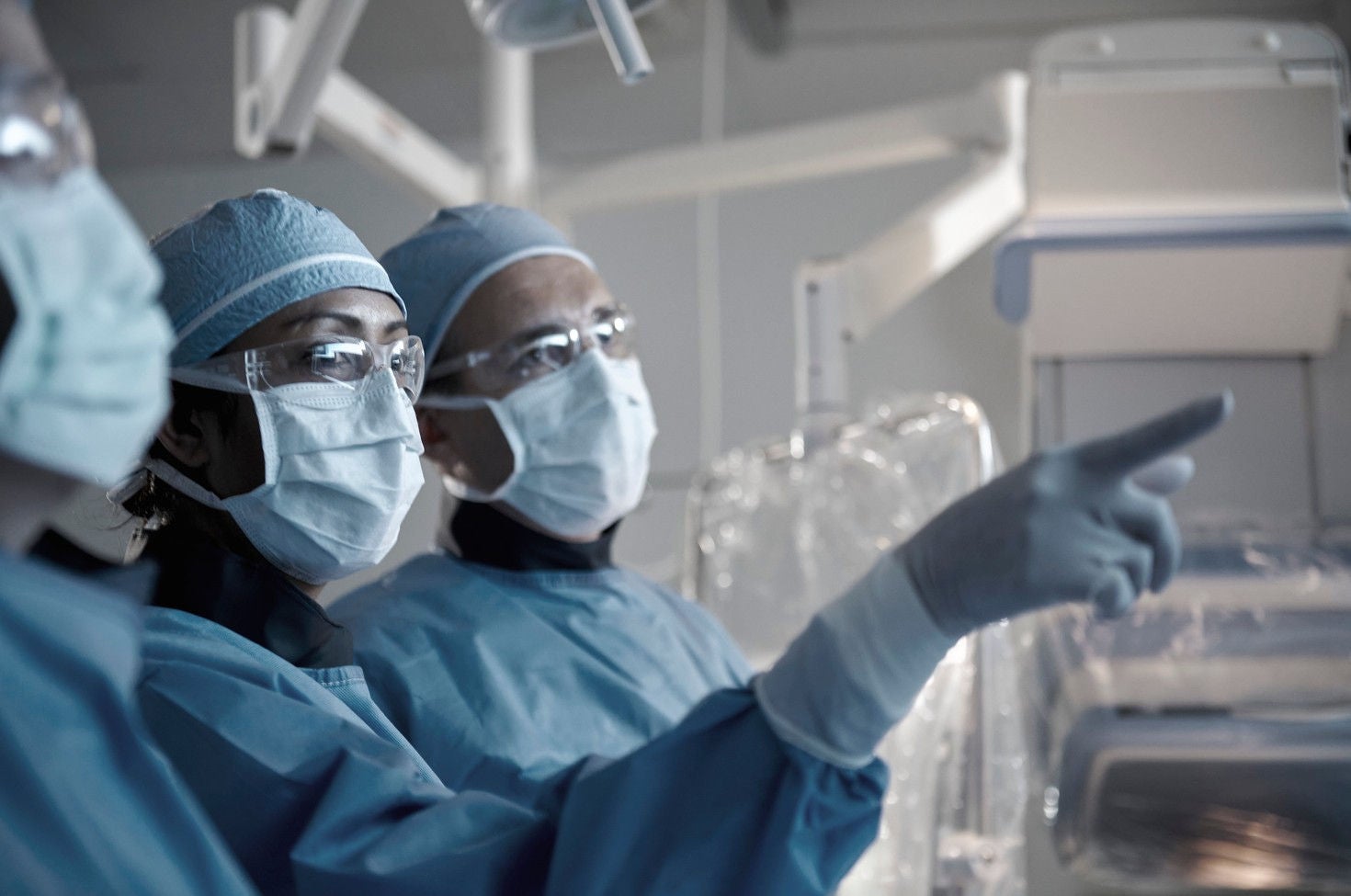 A group of medical professionals dressed in blue surgical gowns and masks are seen inside a modern operating room.