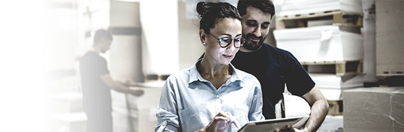 Man and woman in warehouse looking at a tablet the woman uses.