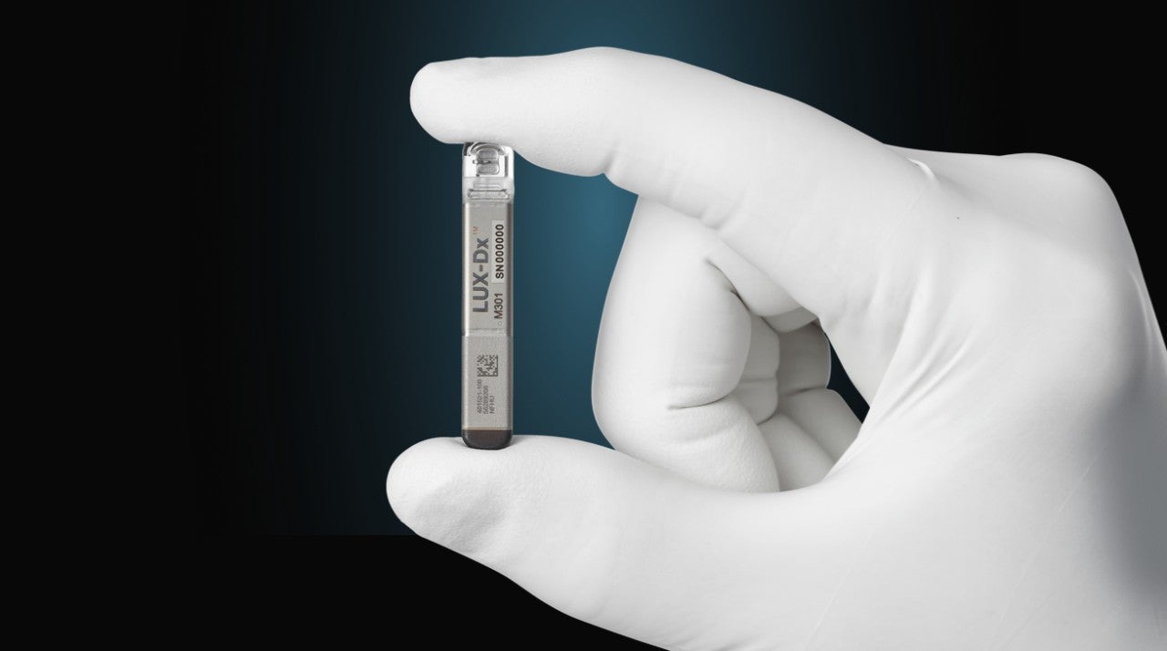 A close-up of the Lux-Dx™ device being held with a gloved hand. 