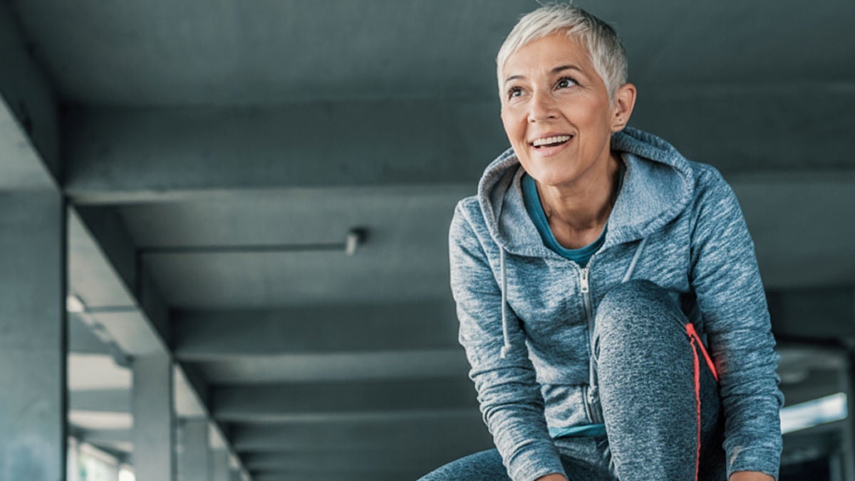 Person smiling and bending forward in athletic wear under shaded structure.