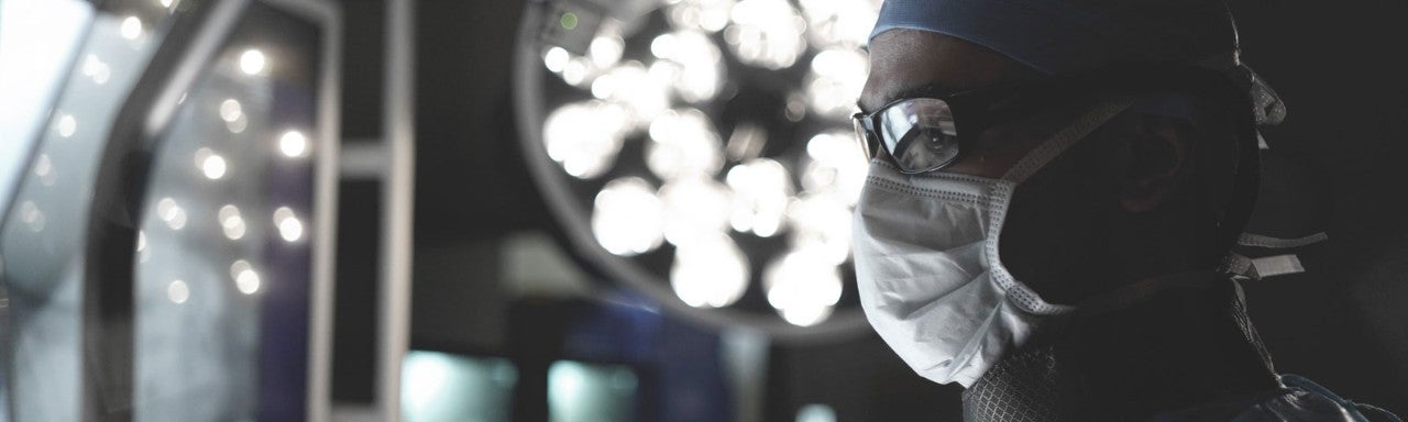 Healthcare provider in surgical mask, cap and eye protection looking slightly upward,